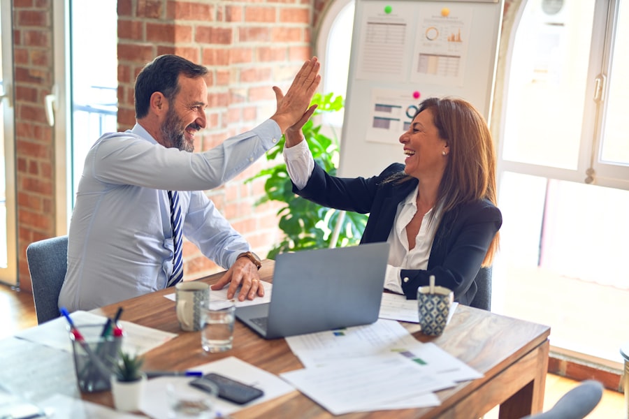 Two colleagues high-fiving over a laptop and paperwork in a bright office